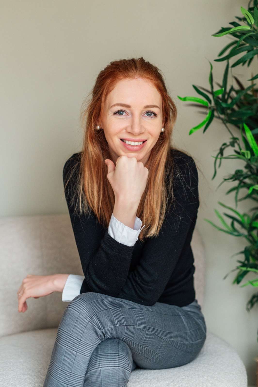 Marjolein Ligtvoet zit op een lichte bank met haar kin op haar hand en glimlacht in de camera. Naast haar een groene plant.