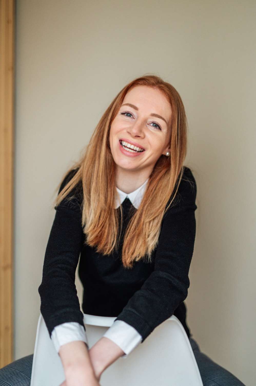 Marjolein Ligtvoet zit achterstevoren op een witte stoel en lacht, haar hoofd een beetje schuin.